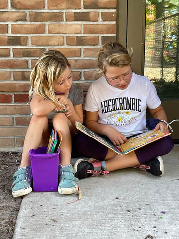 two girls sitting outside reading a book